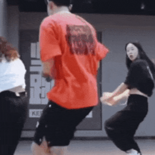 a man in a red shirt is dancing with two women in black pants