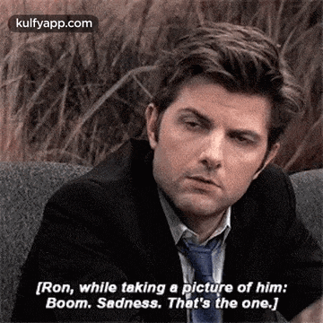 a man in a suit and tie is sitting on a couch talking to another man .
