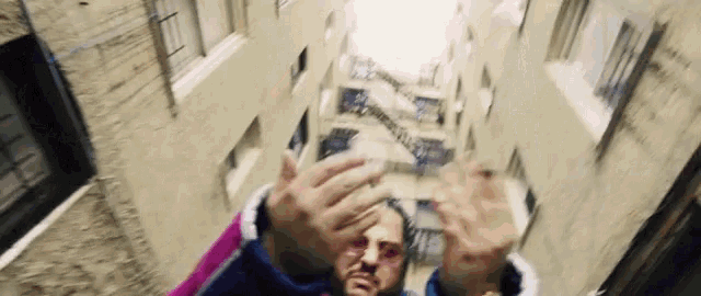 a man is standing in a narrow alleyway between two buildings covering his face with his hands .