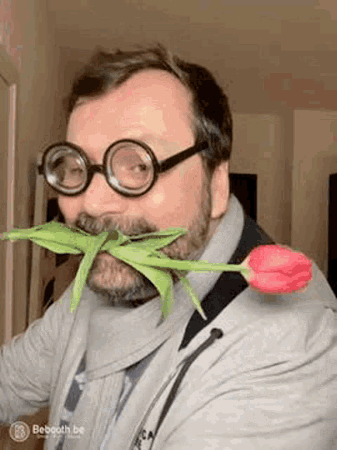 a man wearing glasses and holding a flower in his mouth .