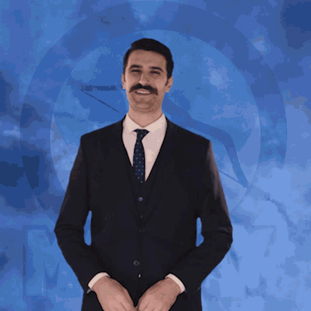 a man in a suit and tie is smiling in front of a blue background with the letter m on it