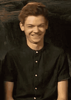a young man in a black shirt is smiling while sitting on a couch .