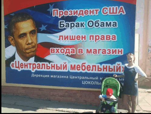 a woman holding a baby in front of a billboard with barack obama on it