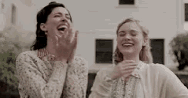 two women are laughing together while standing next to each other .