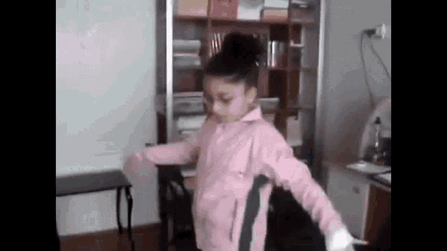 a girl in a pink jacket is dancing in a room