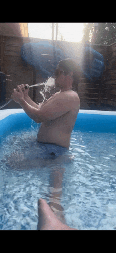 a shirtless man is sitting in a pool drinking from a bottle