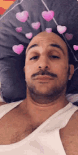 a man in a white tank top is laying on a bed with hearts on his head