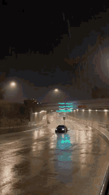 a car is driving down a wet highway at night under a bridge