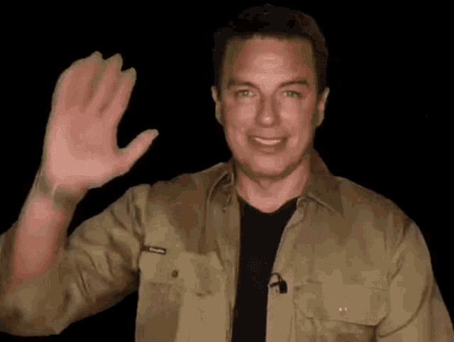 a man in a khaki shirt is waving his hand in the dark .