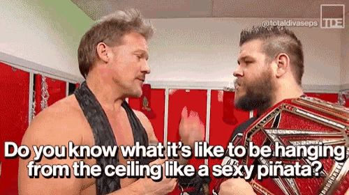 two wrestlers are talking to each other in a locker room and one of them is wearing a championship belt .