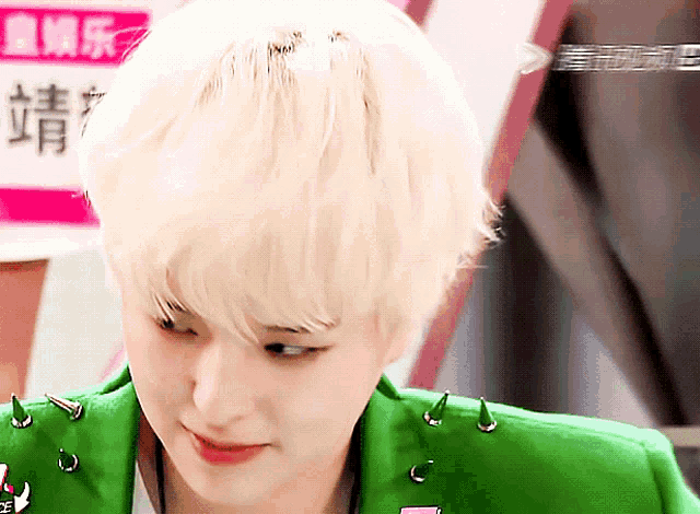 a woman with blonde hair is wearing a green jacket with spikes
