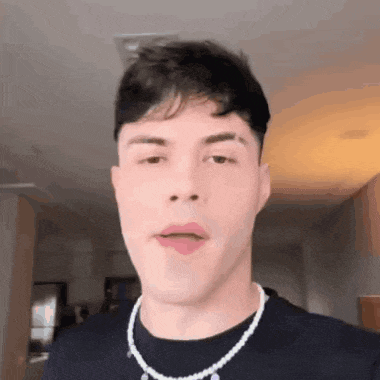 a young man wearing a pearl necklace is looking at the camera .