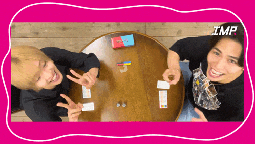 two men are sitting at a table playing a game with the word imp on the bottom right