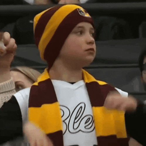 a young boy wearing a maroon and yellow scarf and a white shirt with the word ble on it