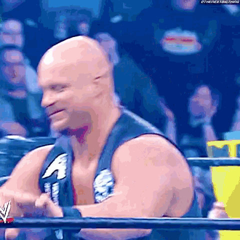 a bald wrestler is standing in a wrestling ring with a crowd watching .