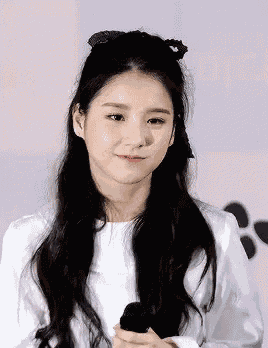 a young woman with long black hair is holding a microphone and wearing a white shirt .