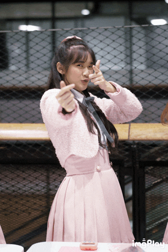 a girl in a pink dress making a heart with her hands