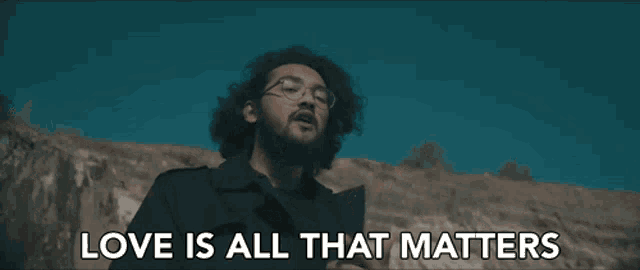 a man with glasses and a beard is standing in front of a mountain and says love is all that matters .