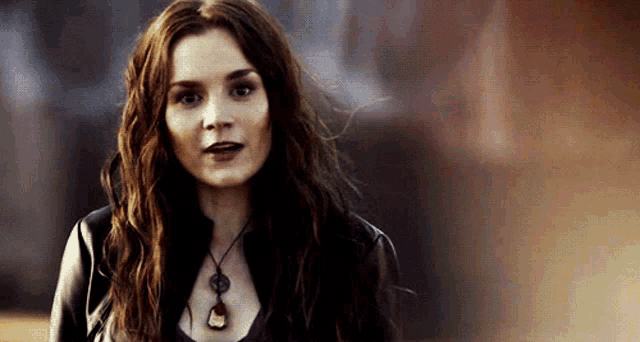 a woman with long red hair wearing a black jacket and a necklace .