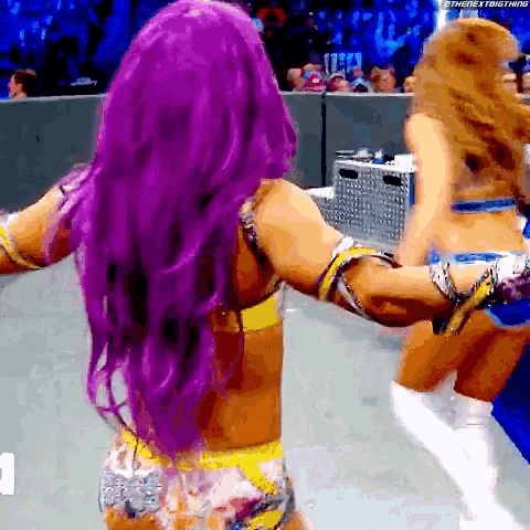 a woman with purple hair is dancing with another woman in a wrestling ring .