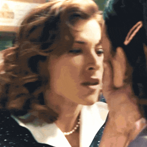 a woman whispering into another woman 's ear