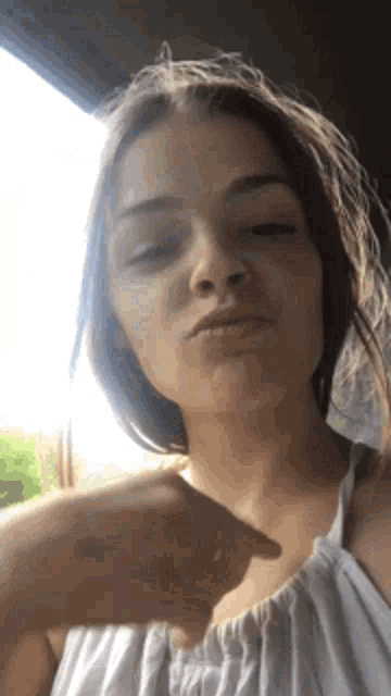 a woman in a white dress is making a funny face while pointing at the camera .
