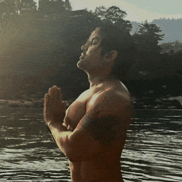 a man with a tattoo on his arm stands in the water with his hands folded in prayer