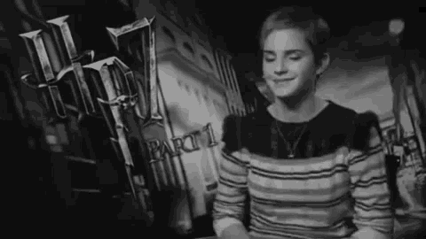 a black and white photo of a woman in a striped shirt standing in front of a harry potter poster .