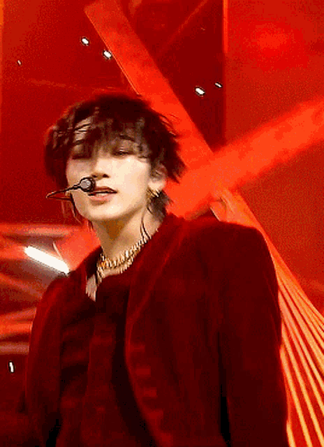 a man wearing a red jacket and a gold necklace is singing into a microphone on a stage