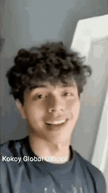 a young man with curly hair is smiling for the camera .