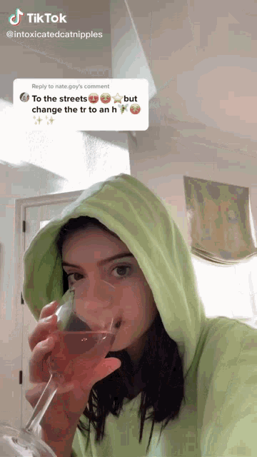 a woman in a green hoodie is drinking a glass of wine from a glass