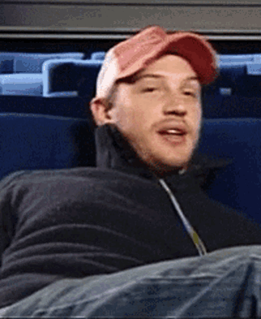 a man wearing a red hat and a black jacket sits in a blue chair