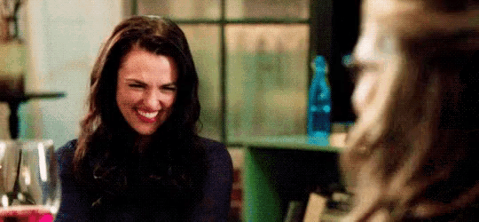 a woman is smiling and laughing while sitting at a table with a glass of wine .