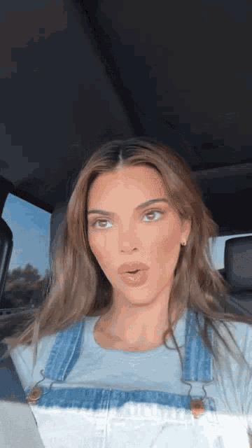 a woman wearing overalls is sitting in a car .