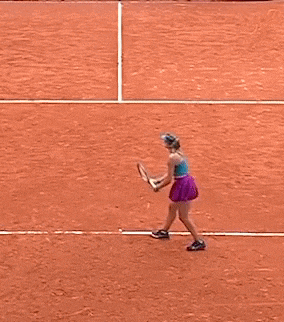 a woman in a blue top and purple skirt is playing tennis on a red court .