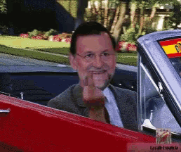 a man in a suit and tie is sitting in a red car and giving the middle finger