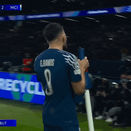 a soccer player holds a flag in front of a scoreboard that says 2 mci on it