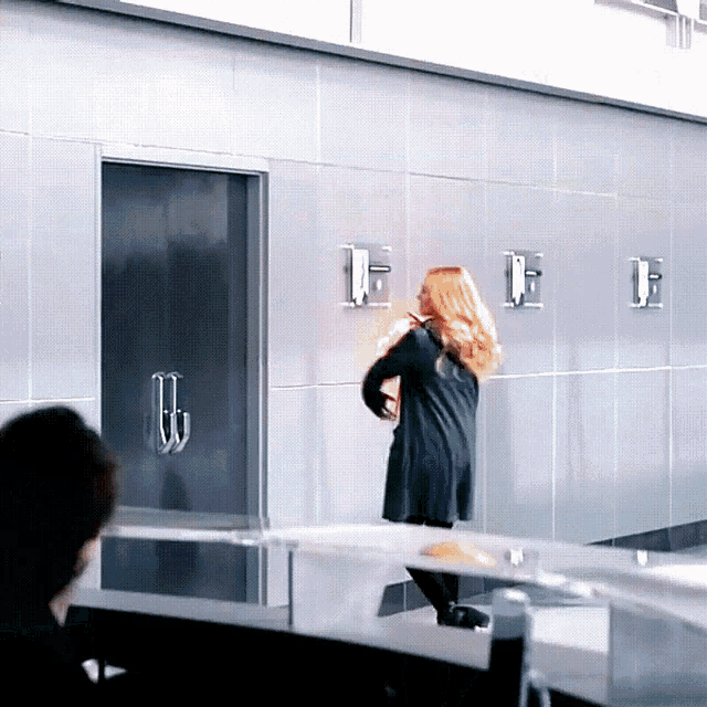 a woman in a black dress stands in front of a wall with letters e and f on it