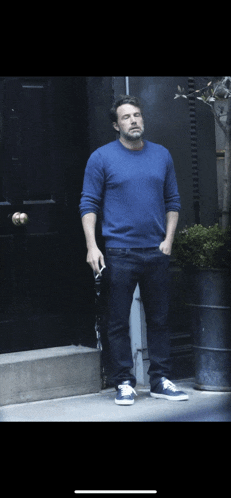 a man in a blue sweater is smoking a cigarette in front of a black door
