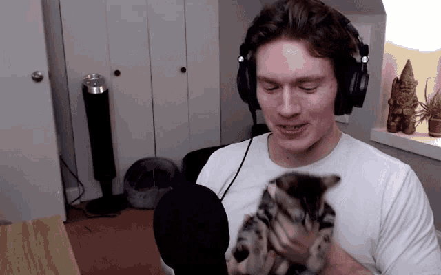 a man wearing headphones holds a kitten in his arms