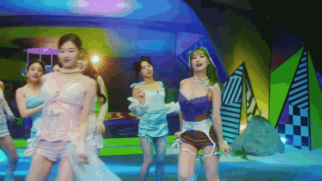 a group of women are dancing on a stage in front of a colorful background