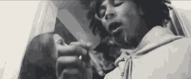 a black and white photo of a man and a woman smoking a cigarette in a room .