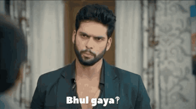 a man with a beard is wearing a black suit and a black shirt and says bhul gaya ?