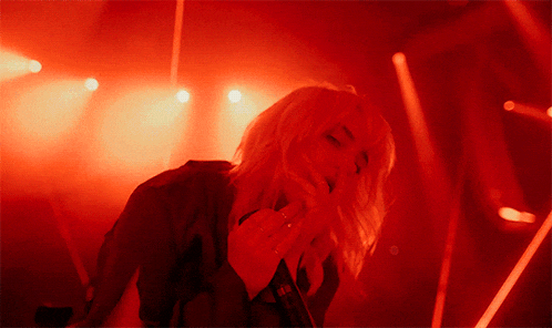 a woman singing into a microphone in a dark room with red lights
