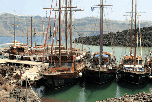 a row of boats are docked in a harbor and one of them has a greek flag flying on the mast