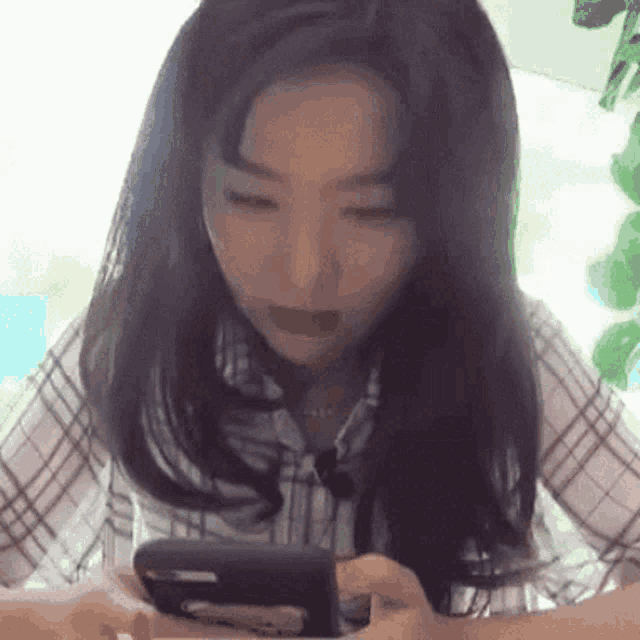 a woman in a plaid shirt is looking at her phone .