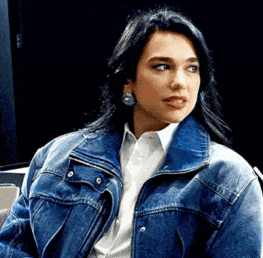 a woman wearing a denim jacket and a white shirt is sitting in a chair .