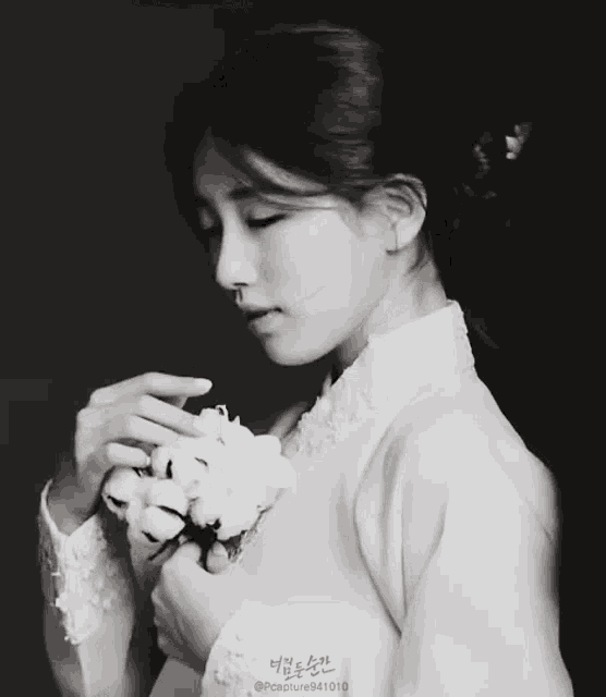 a woman in a white dress is holding a flower in her hands .