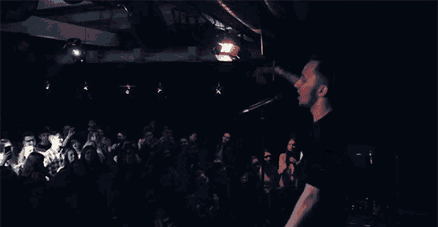 a man singing into a microphone with a crowd watching