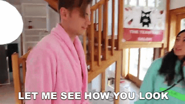 a man in a pink robe is standing next to a woman in a green sweater and says let me see how you look .